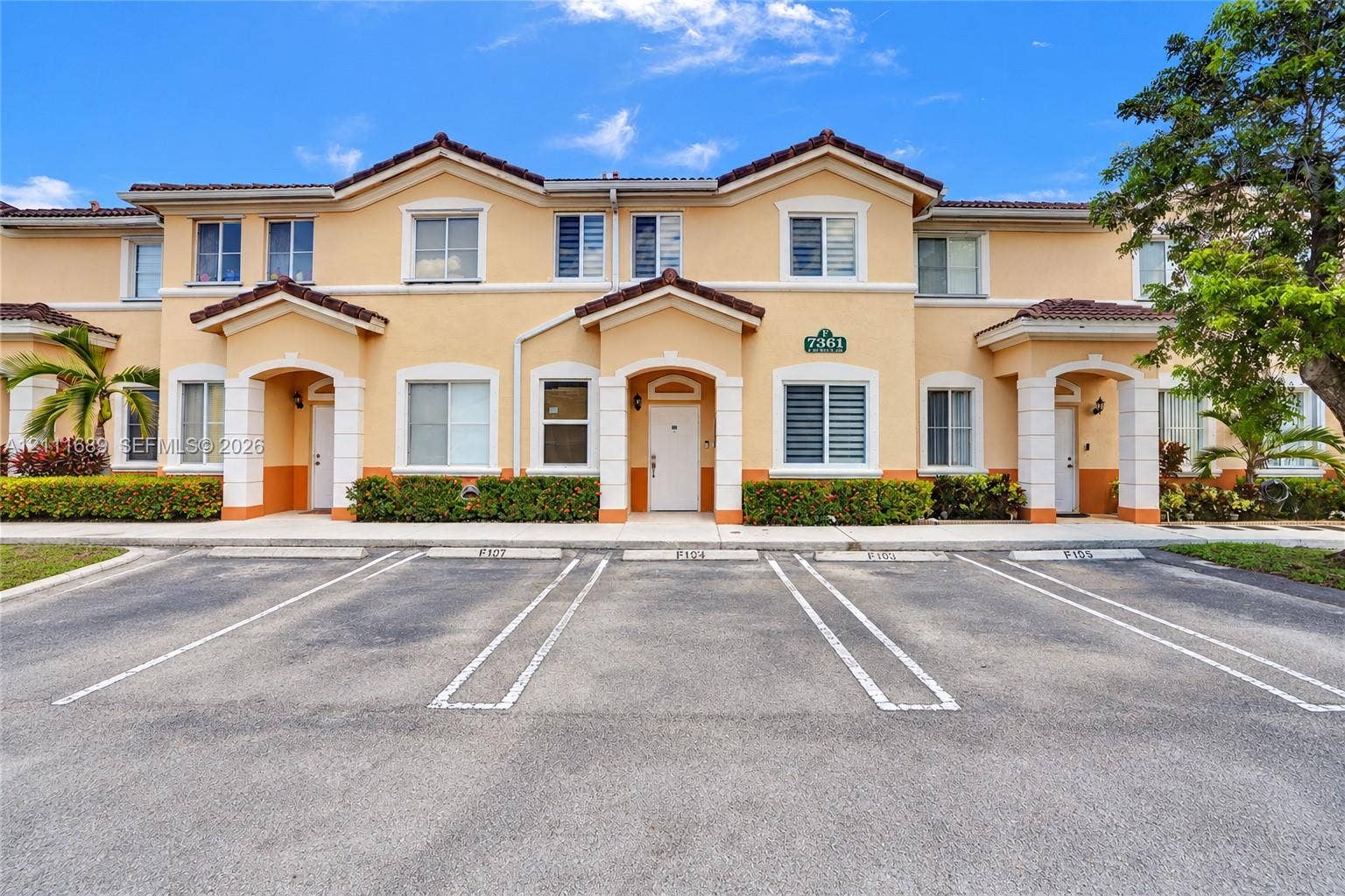 7305 NW 174th Terrace, #103, Hialeah, FL 33015 Two-story exterior featuring a stucco faade, gabled rooflines, covered entryways with columns, and dedicated asphalt parking spaces