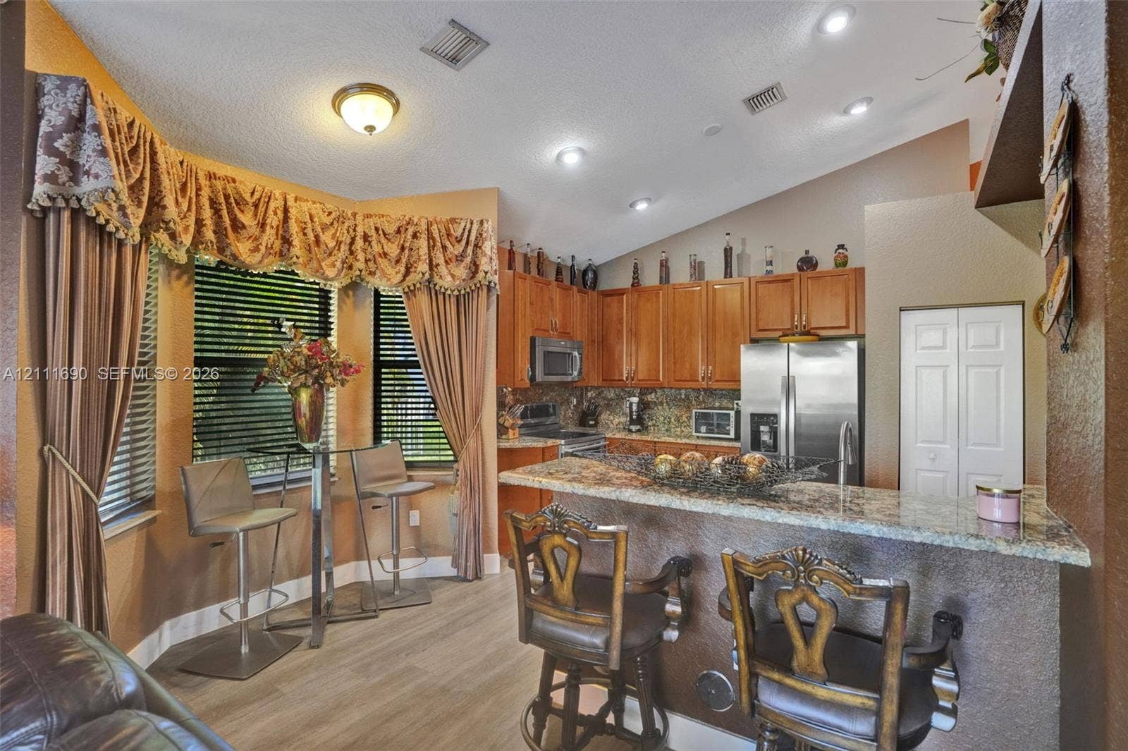 Kitchen featuring wood cabinetry, stone-surface breakfast bar, recessed lighting, and bay windows