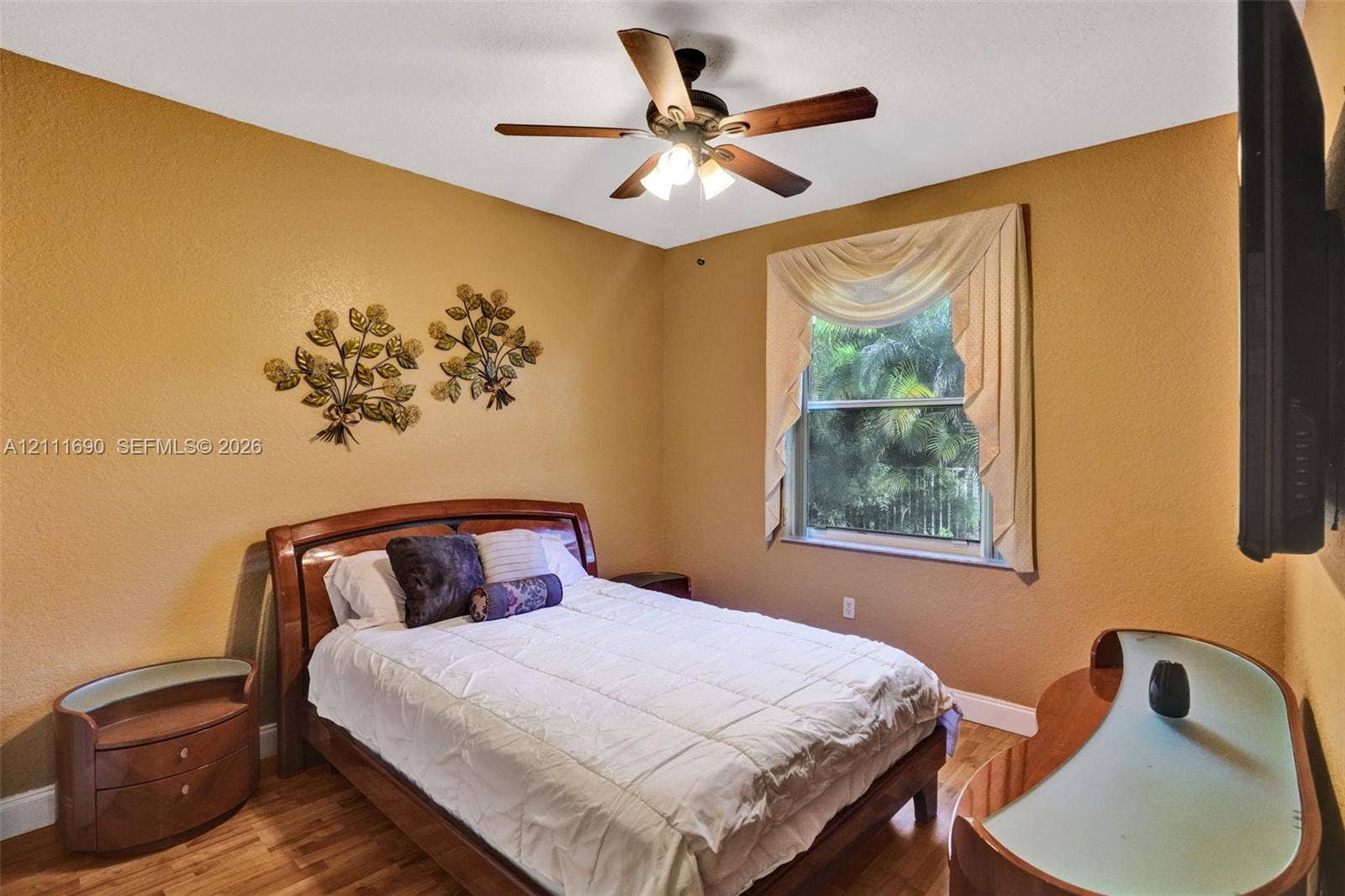 Room featuring wood-finish flooring, a ceiling fan with integrated lighting, and a window with exterior greenery