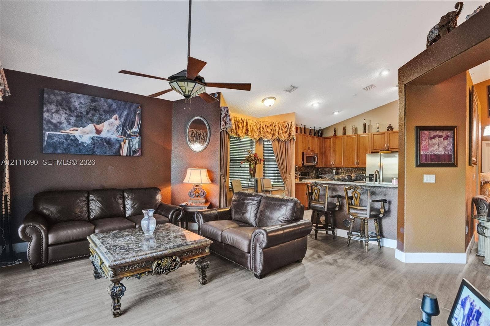 Vaulted ceiling with an integrated ceiling fan, wood-finish flooring, and a kitchen peninsula with a breakfast bar