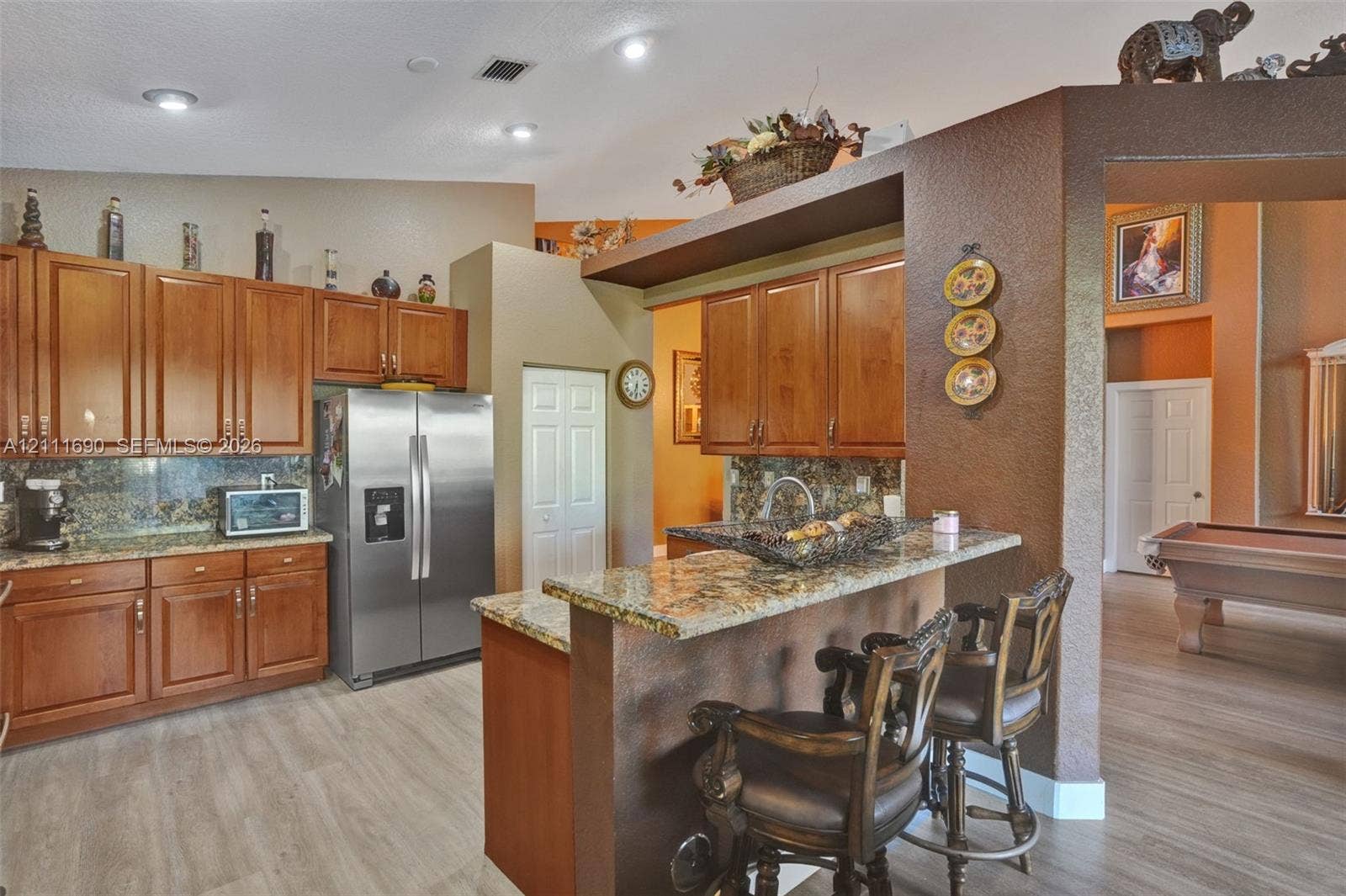 Kitchen featuring wood cabinetry, stone-finish countertops, stainless steel refrigerator, and a breakfast bar