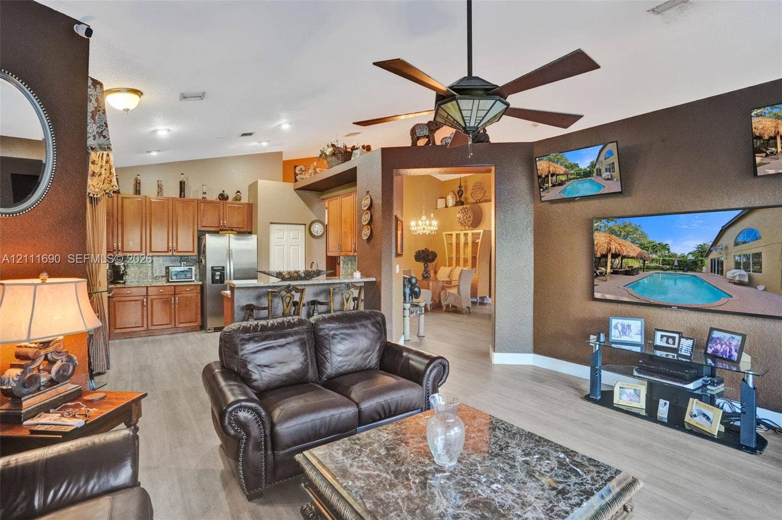 Open concept layout featuring wood-finish flooring, vaulted ceilings with a geometric chandelier ceiling fan, and kitchen cabinetry with a breakfast bar