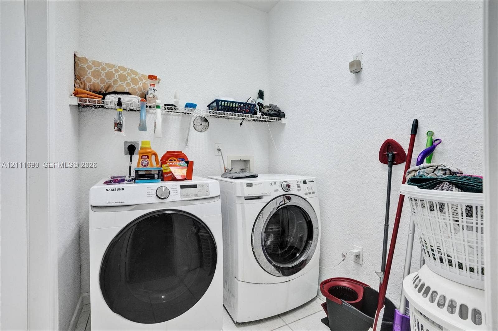 Laundry area featuring white ceramic tile flooring and white wall-mounted wire shelving