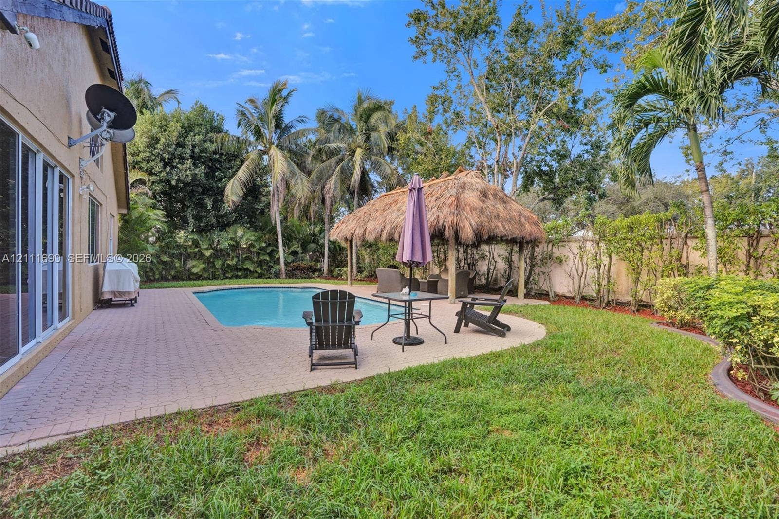 Backyard area featuring an in-ground swimming pool, a thatched-roof palapa, paver patio, and mature palm trees