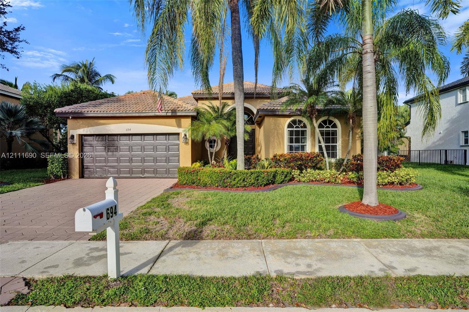 Single-story exterior featuring a tile roof, stucco finish, arched windows, and a paved driveway leading to a two-car garage