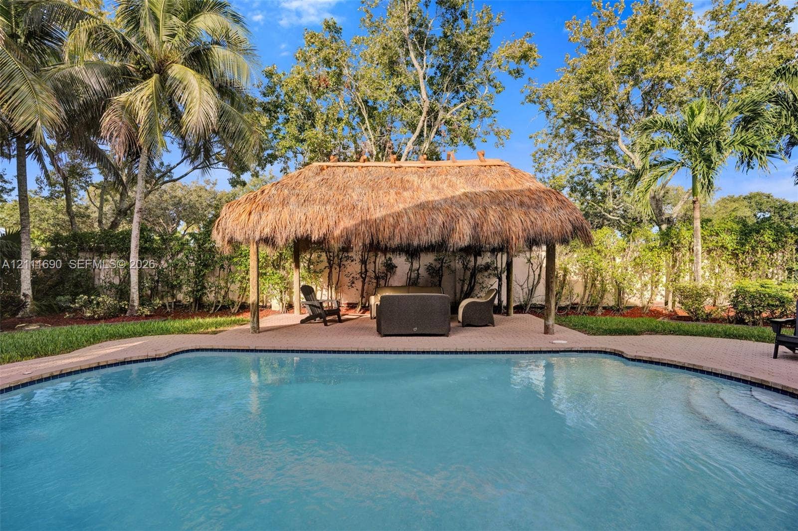 In-ground swimming pool with paver decking and a thatched-roof tiki hut