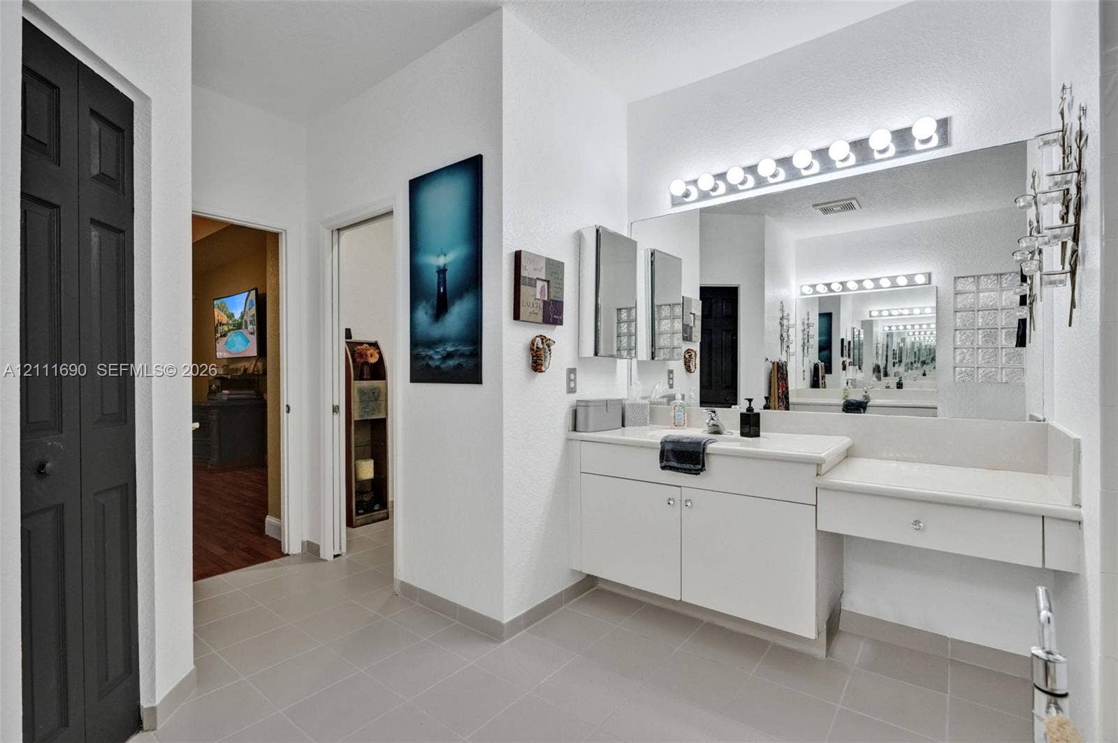 Bathroom featuring a vanity with integrated sink and stone-finish countertop, dual-cabinet storage, full-width mirror, multi-bulb overhead vanity lighting, and ceramic tile flooring