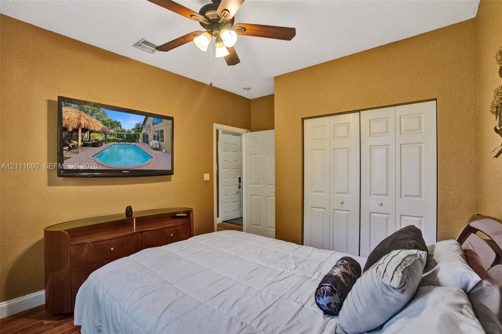 Room featuring textured wall finishes, wood-finish flooring, a ceiling-mounted light fixture with a fan, and dual-panel closet doors