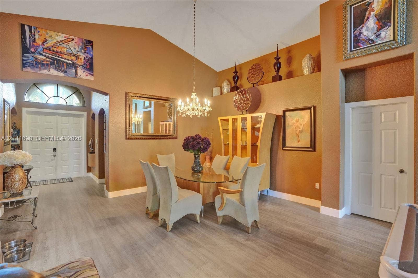 Vaulted ceilings featuring decorative architectural niches, wood-finish flooring, double-door entry with arched transom window, and a multi-light crystal chandelier