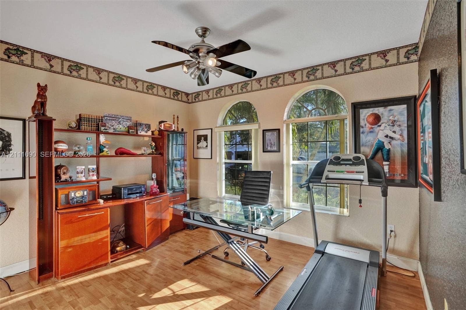 Room featuring wood-finish flooring, dual arched windows, and a ceiling fan with integrated lighting
