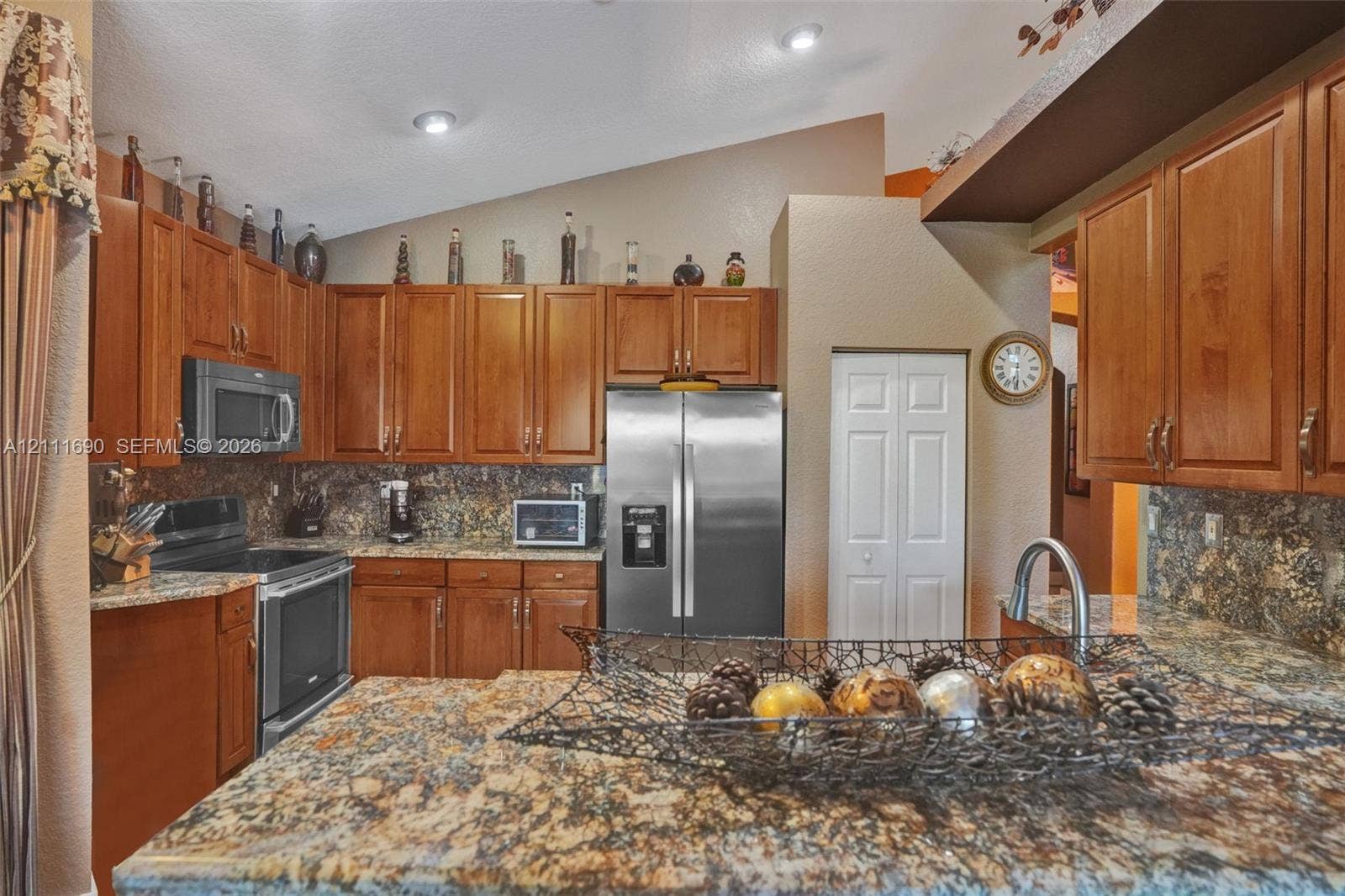 Kitchen featuring stained wood cabinetry, stone-surface countertops, stone-tile backsplash, stainless steel appliances, and vaulted ceiling