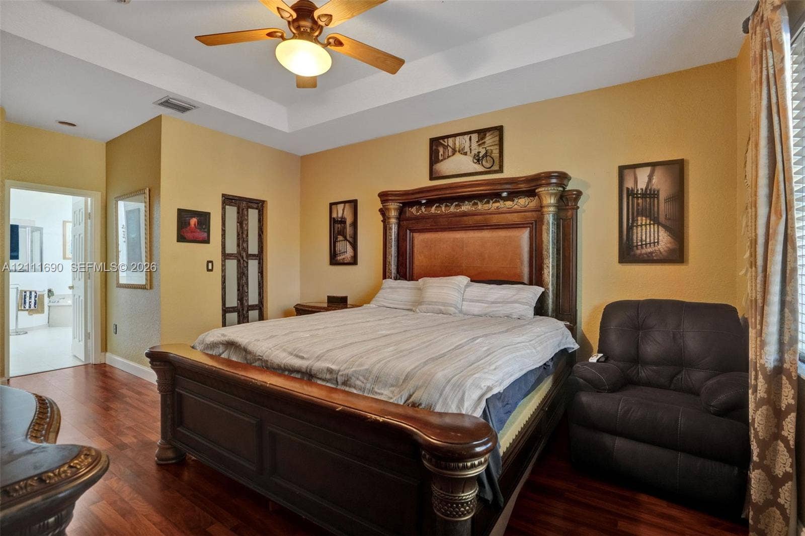Tray ceiling, wood-finish flooring, ceiling fan with integrated light fixture, and paneled door