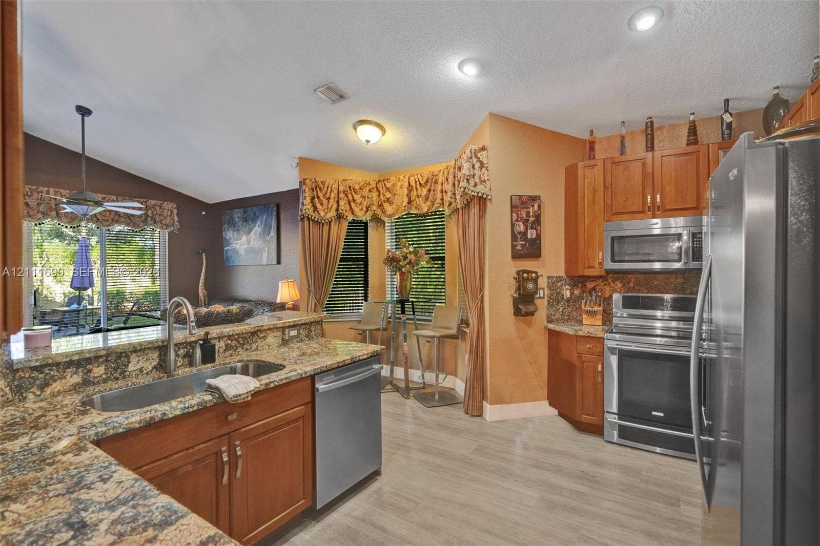 Kitchen featuring stone countertops, stainless steel appliances, wood cabinetry, recessed lighting, and a bay window