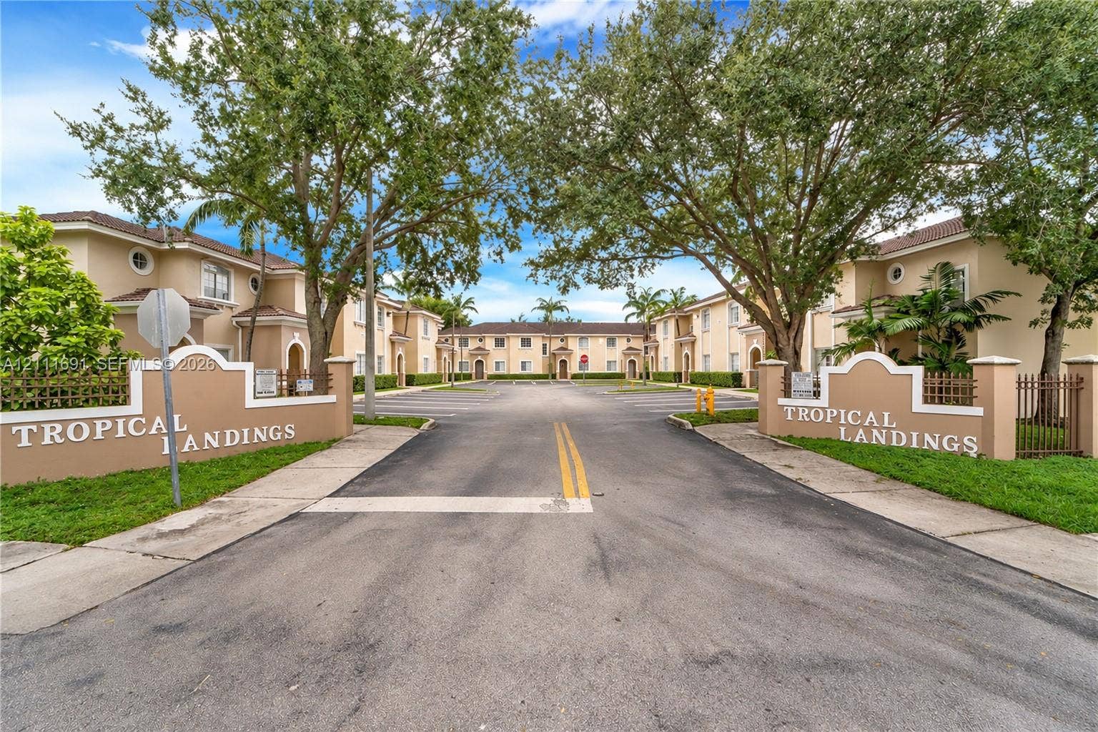 7080 NW 174th Terrace, #201, Hialeah, FL 33015 Stucco exterior multi-unit complex featuring dual monument signage, paved entry drive, and mature tree canopy