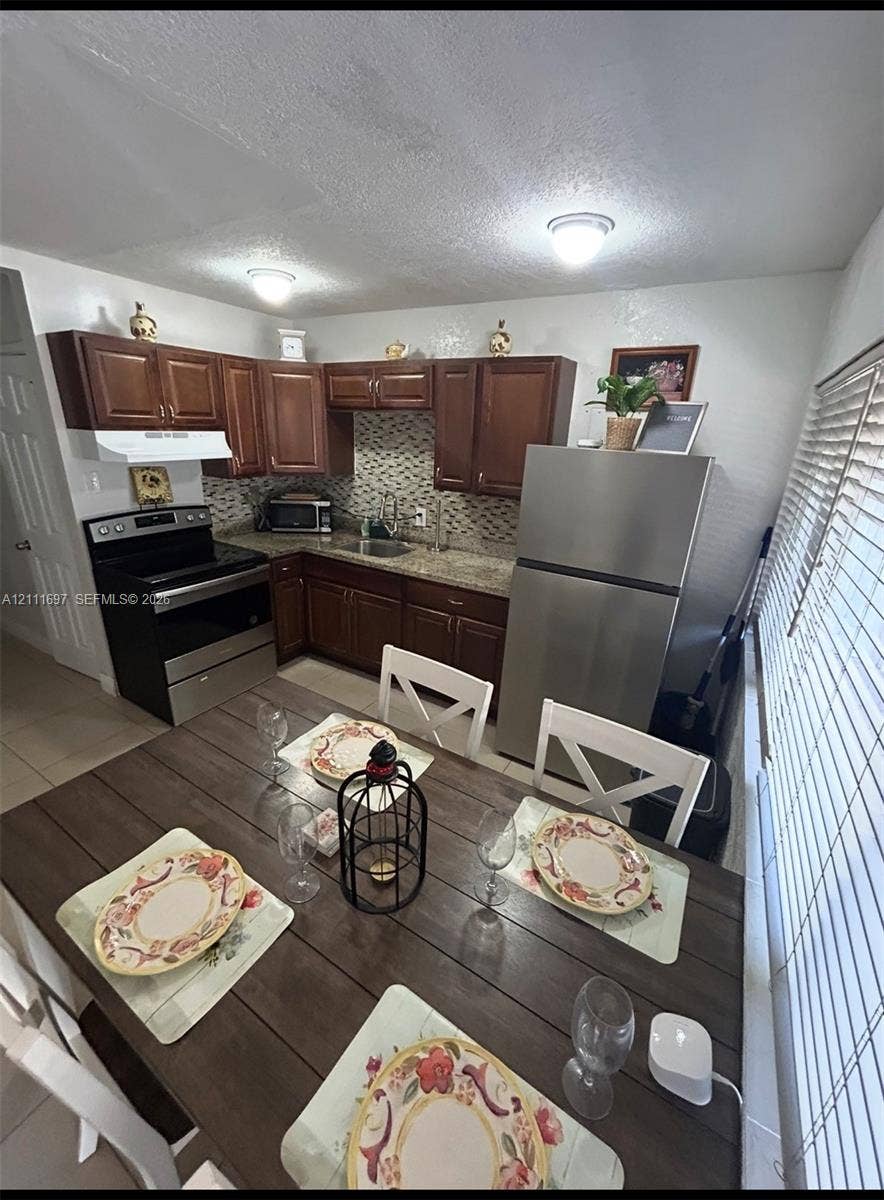 Kitchen featuring dark wood cabinetry, stone-finish countertops, decorative mosaic tile backsplash, and stainless steel appliances