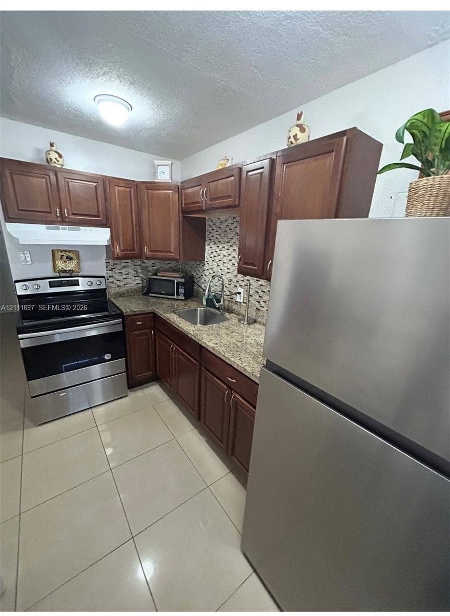 Kitchen featuring raised-panel wood cabinetry, stone-finish countertops, tile backsplash, tile flooring, and stainless steel appliances