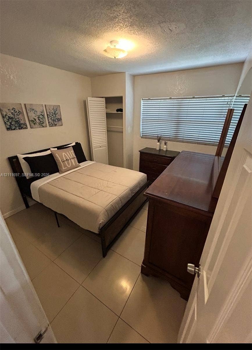 Ceramic tile flooring, neutral wall tones, window blinds, closet with louvered door, and overhead lighting