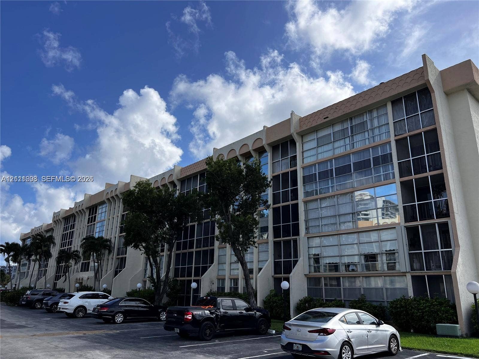 601 Three Islands Boulevard, #308, Hallandale Beach, Hallandale Beach, FL 33009 Mid-rise multi-story building featuring structural concrete columns, expansive glass windows with black framing, and decorative scalloped roofline details