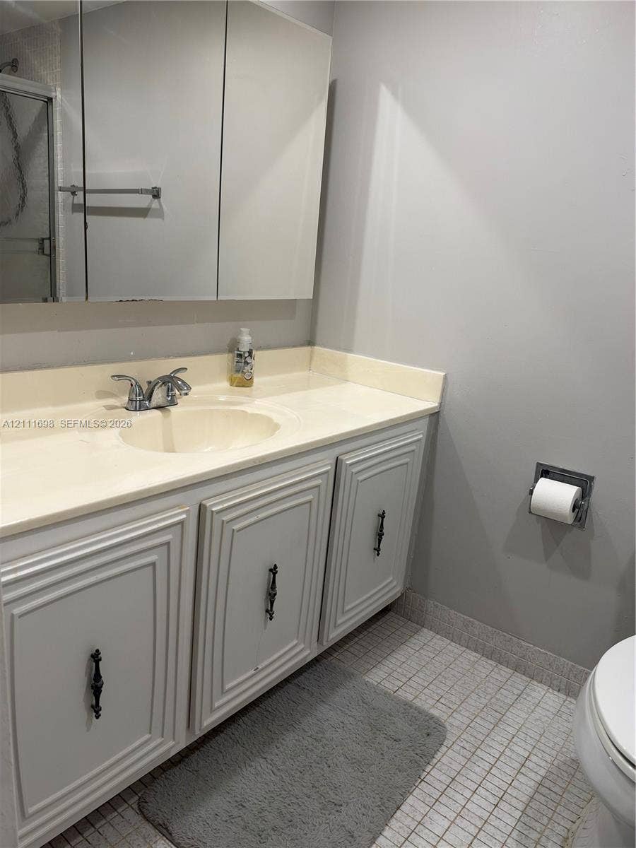 601 Three Islands Boulevard, #308, Hallandale Beach, Hallandale Beach, FL 33009 Bathroom vanity featuring painted cabinetry, a neutral integrated countertop with an oval basin, a chrome dual-handle faucet, and a wall-mounted mirrored medicine cabinet