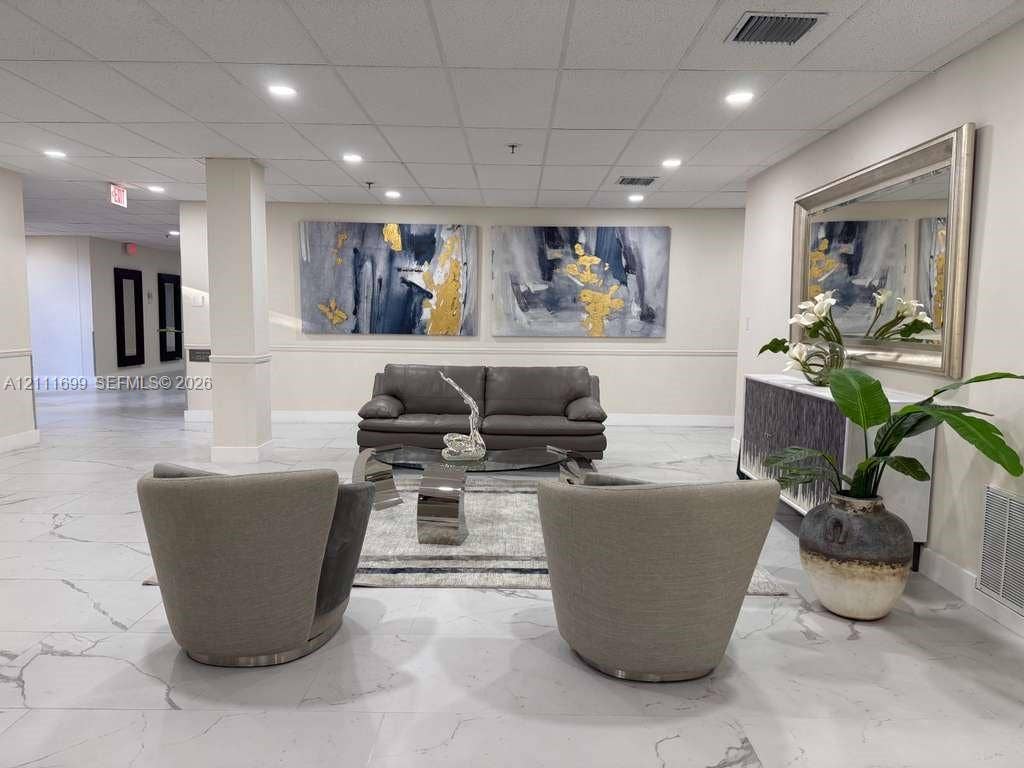 Spacious lobby area featuring large-format stone-patterned tile flooring, a suspended drop ceiling, and recessed lighting