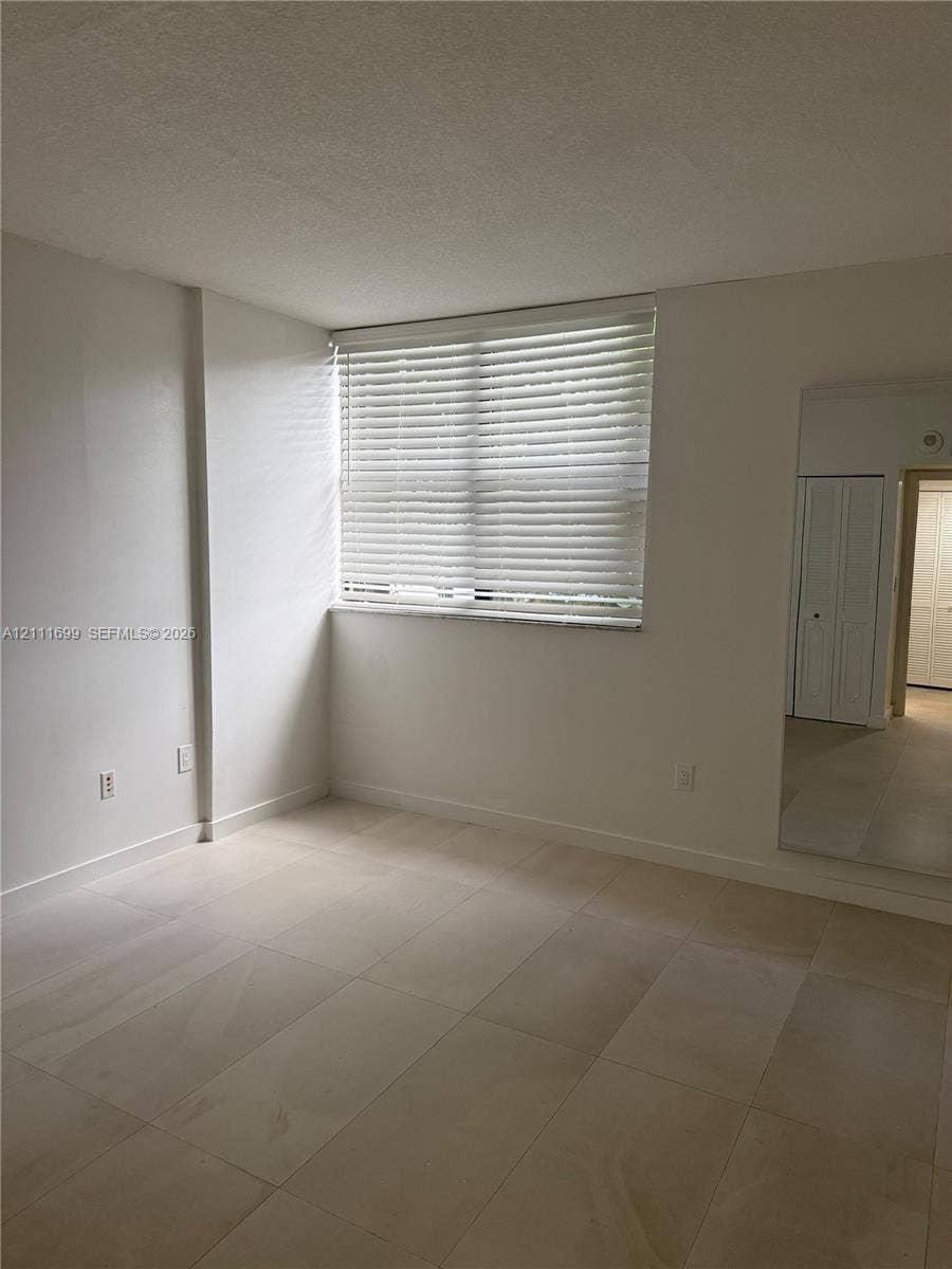 Neutral-toned tile flooring, large window with horizontal blinds, and mirrored closet doors