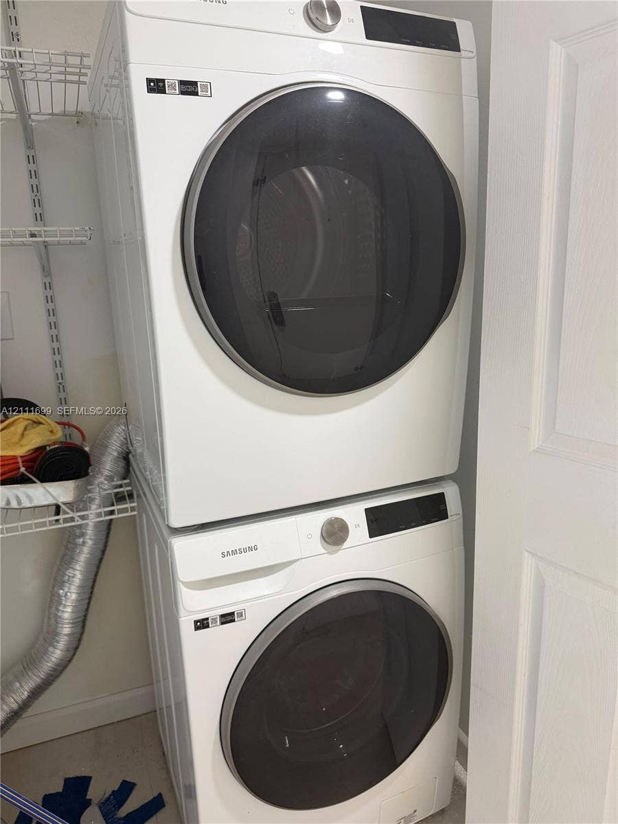 Stacked white front-load washer and dryer unit with metallic circular doors and built-in wire shelving