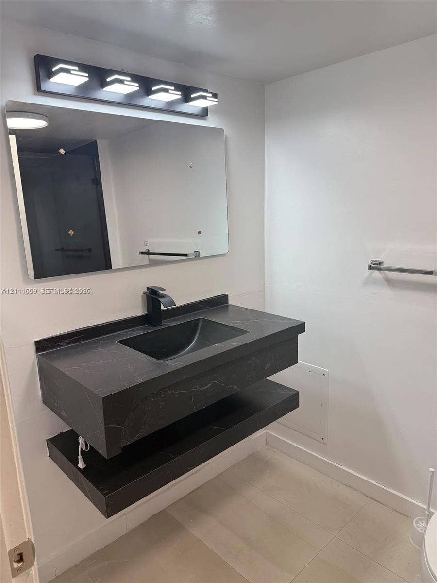 Floating dark stone-finish vanity featuring an integrated rectangular sink, matte black faucet, minimalist four-light vanity fixture, and large rectangular mirror