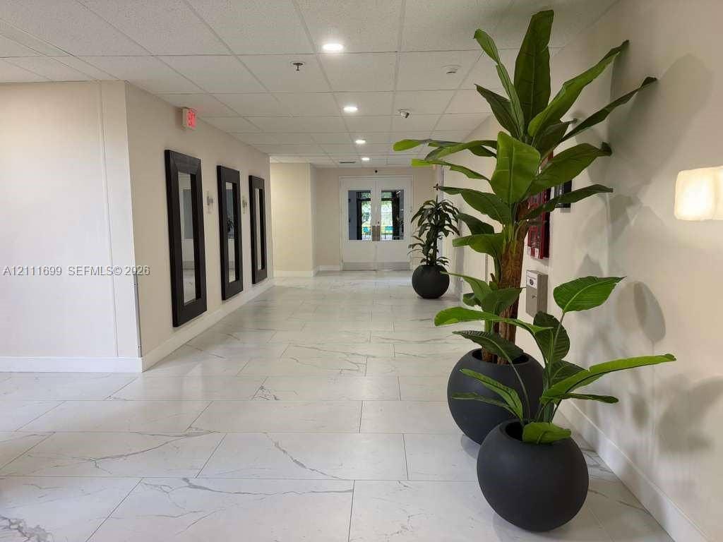 Wide hallway featuring large-format veined tile flooring, recessed ceiling lighting, and three wall-mounted decorative frames