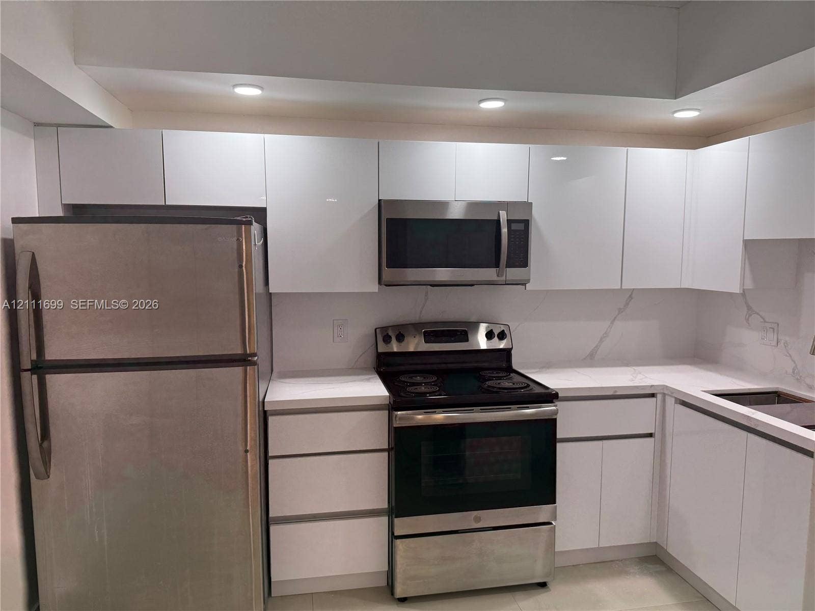Kitchen featuring high-gloss white cabinetry, stone-finish countertops with veining, stainless steel appliances, recessed ceiling lighting, and tile flooring