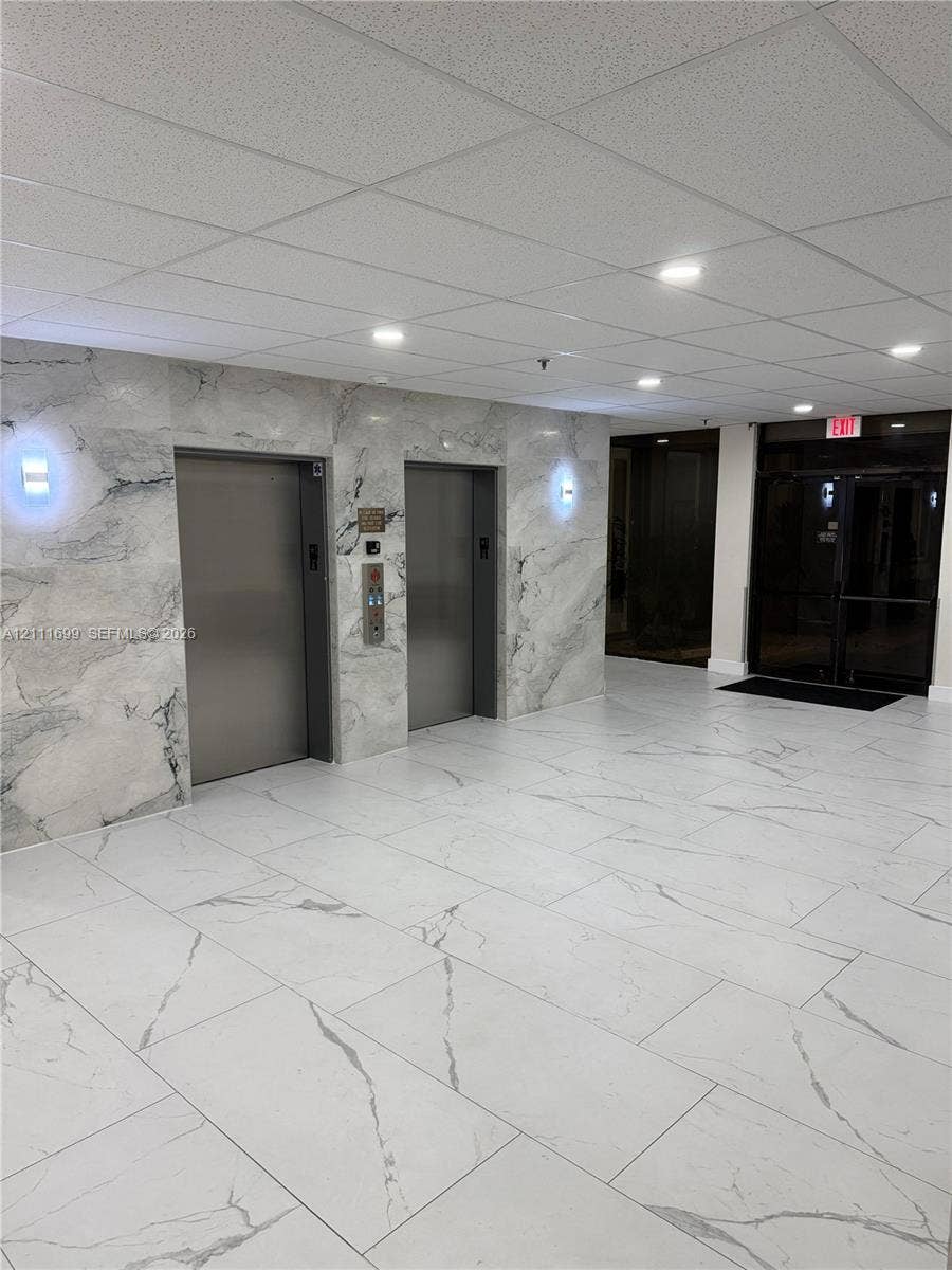 Elevator lobby featuring stone-paneled walls, large-format tiled flooring, recessed ceiling lighting, and dual metallic elevator doors