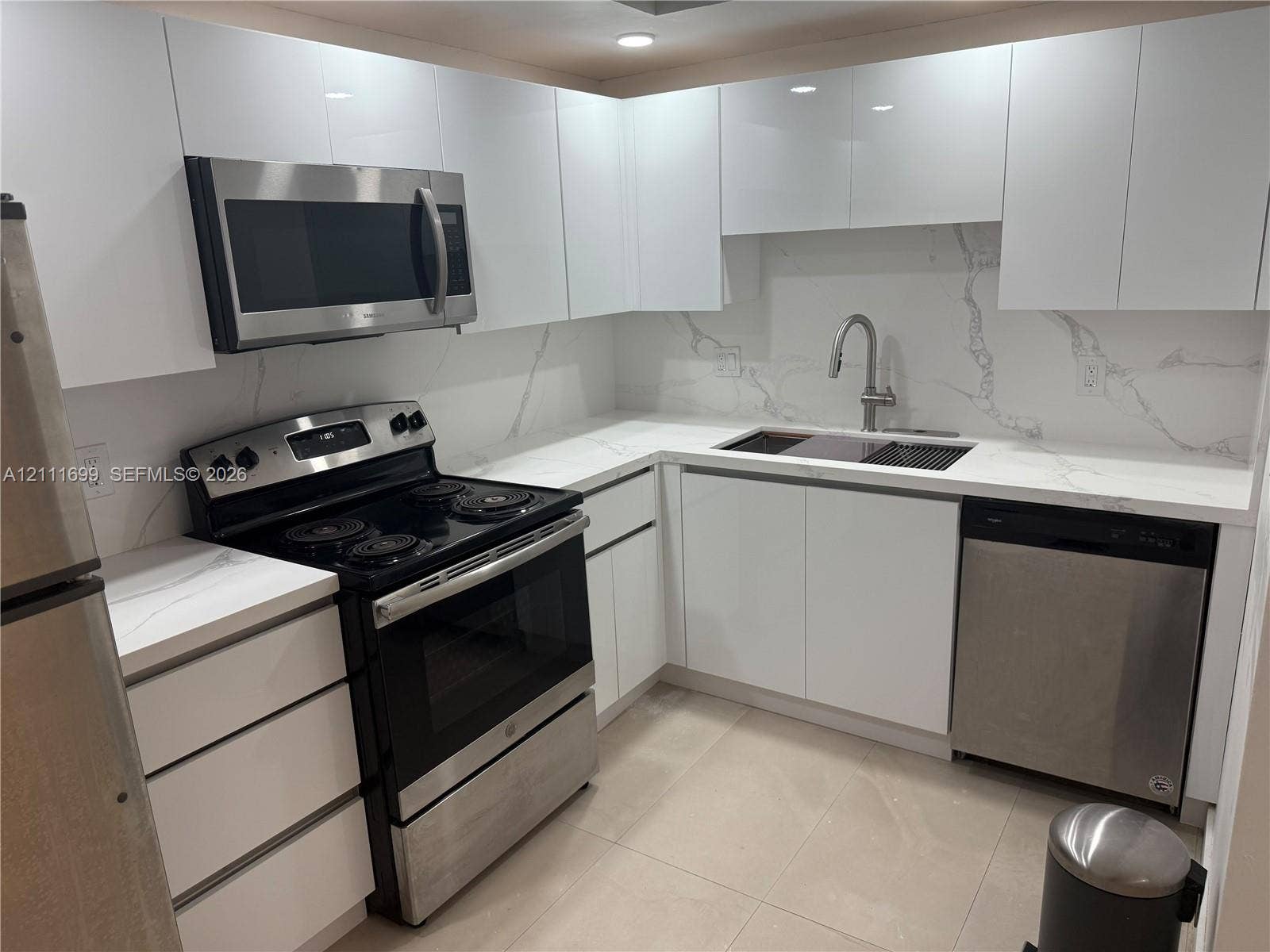 Kitchen featuring high-gloss white cabinetry, stone-surface countertops with backsplash, stainless steel appliances, and a pull-down kitchen faucet