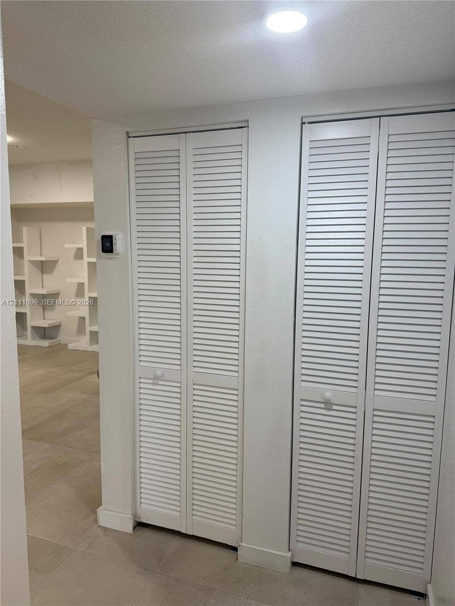 Dual white bi-fold louvered closet doors, neutral tile flooring, and integrated white open-shelf wall cabinetry