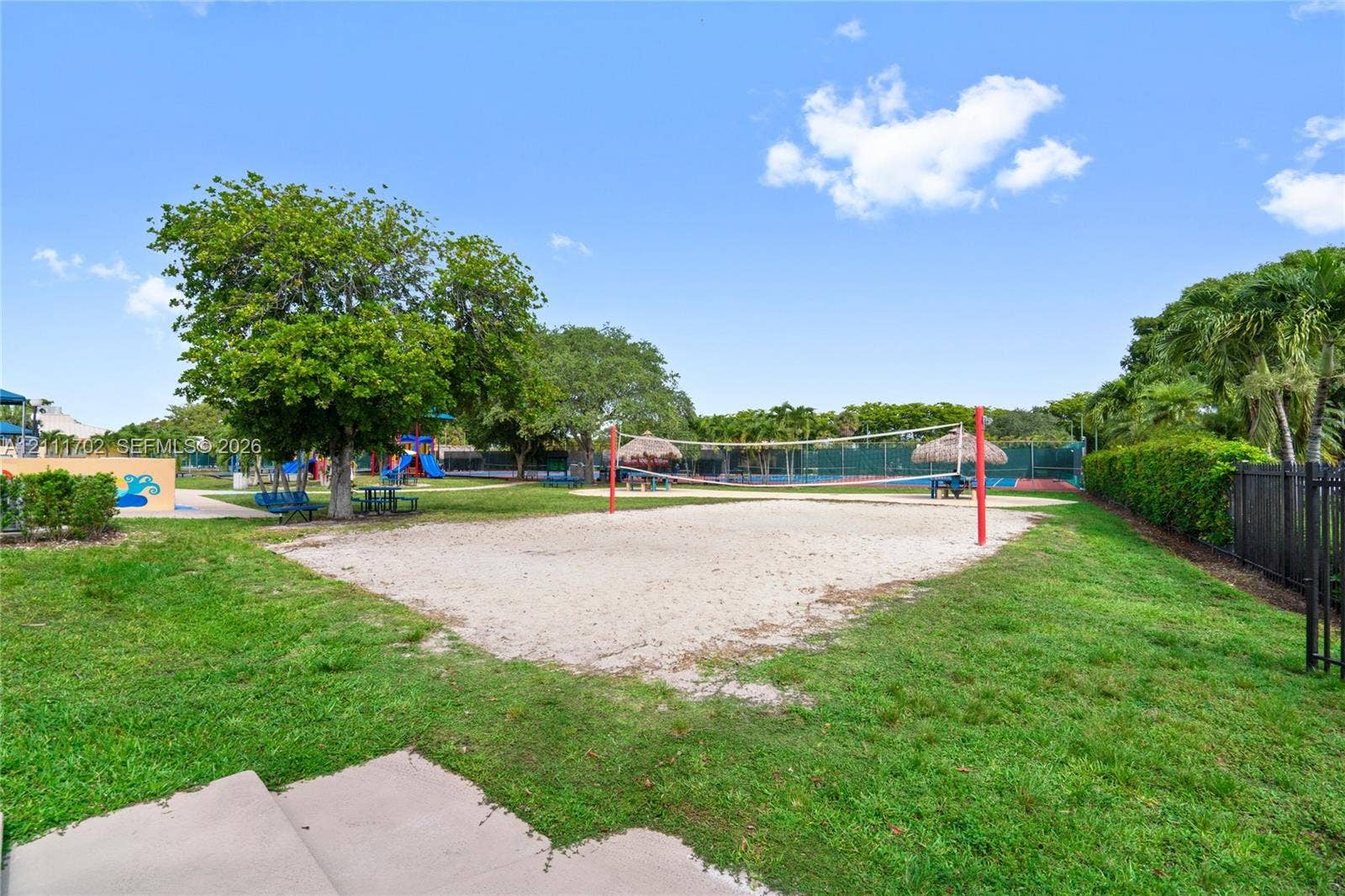 Outdoor recreation area featuring a sand volleyball court, manicured lawn, and mature shade trees
