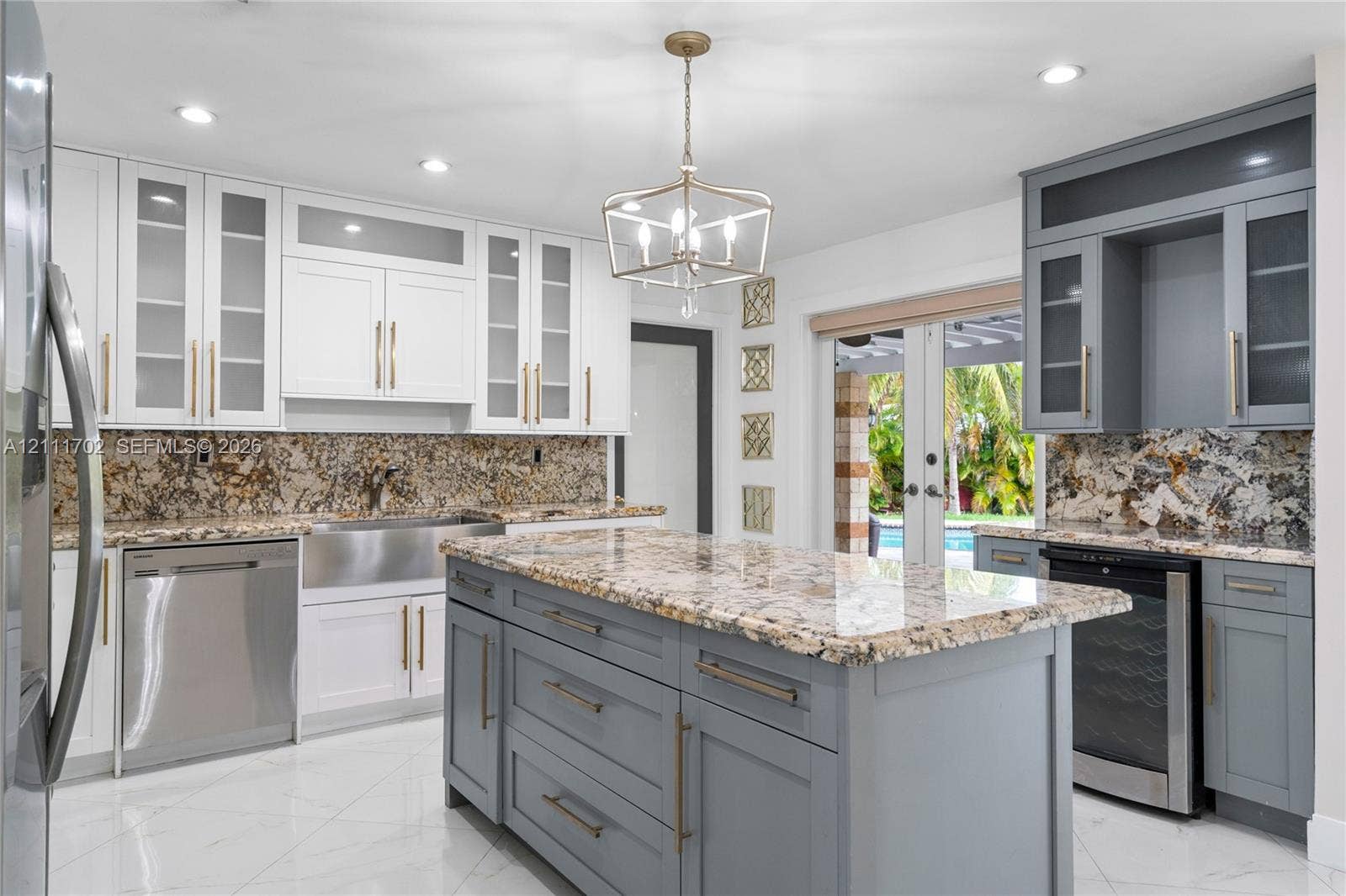 Kitchen featuring two-tone cabinetry with glass-front uppers, a central island with storage, stone countertops, a stainless steel apron-front sink, and large-format tile flooring