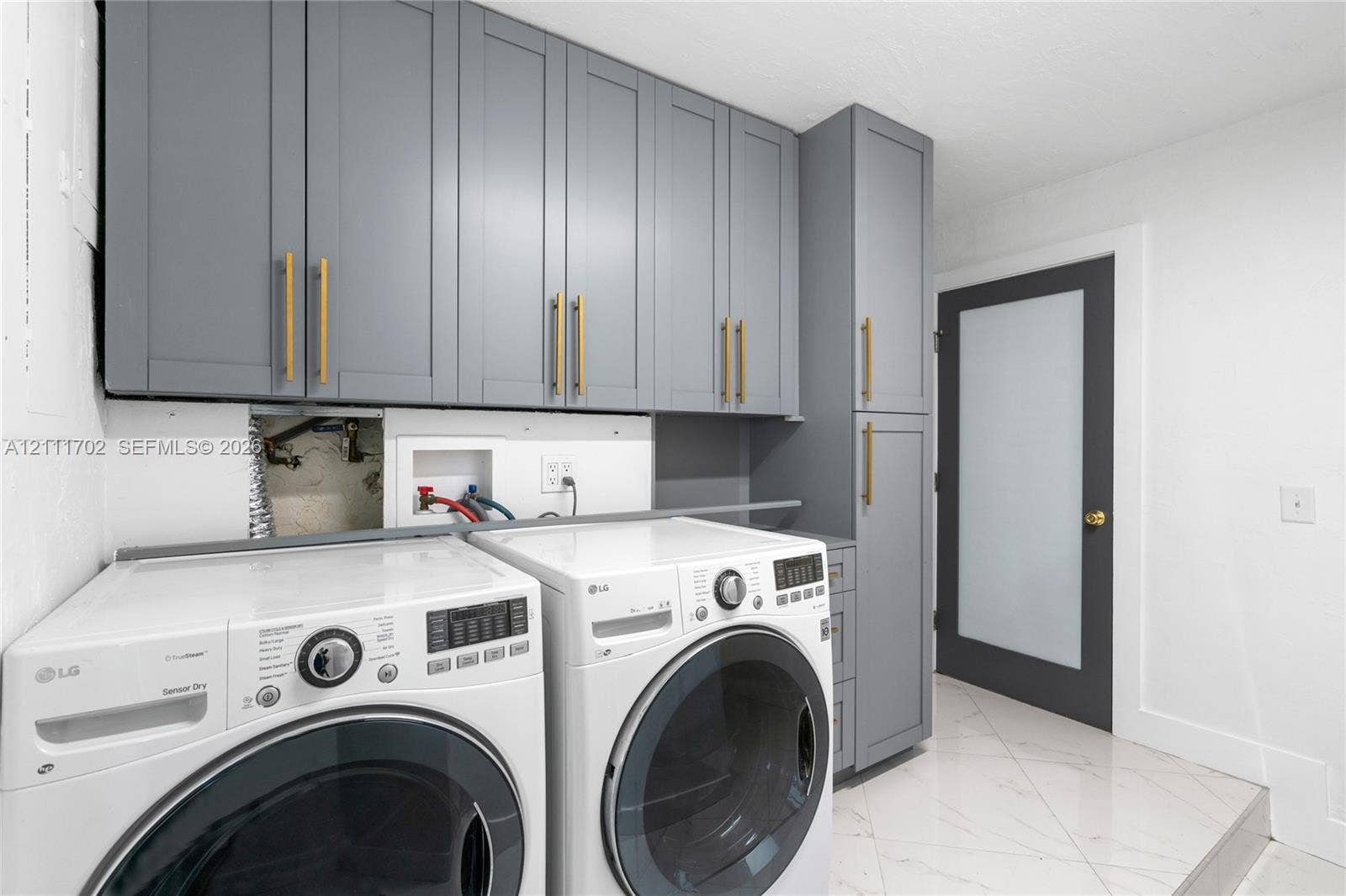 Shaker-style cabinetry in grey featuring vertical gold-tone hardware, full-length pantry cabinet, and a door with a frosted glass panel