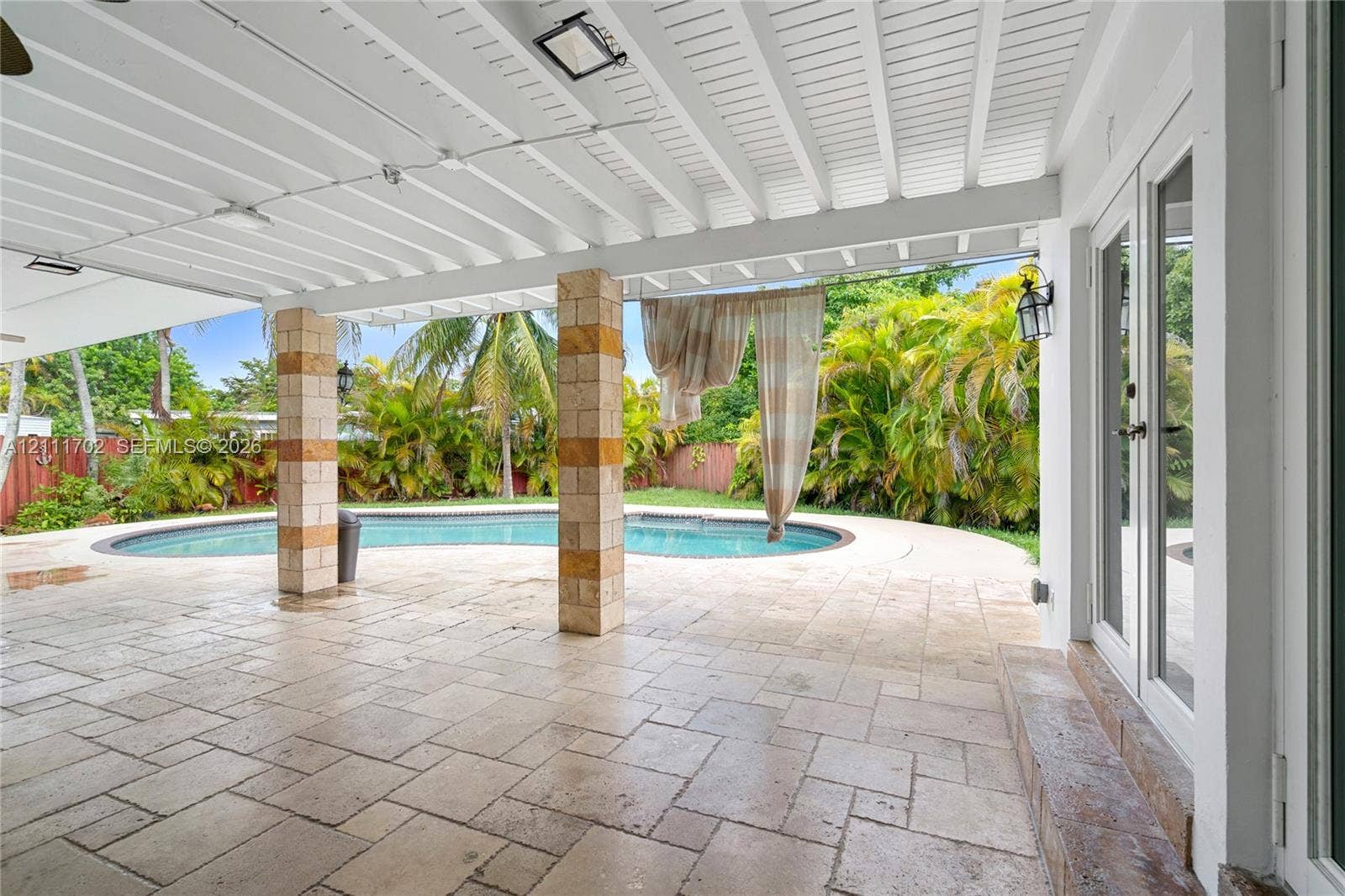 Covered patio featuring stone-tile flooring, vaulted beadboard ceiling, structural stone-clad columns, and a custom-shaped swimming pool