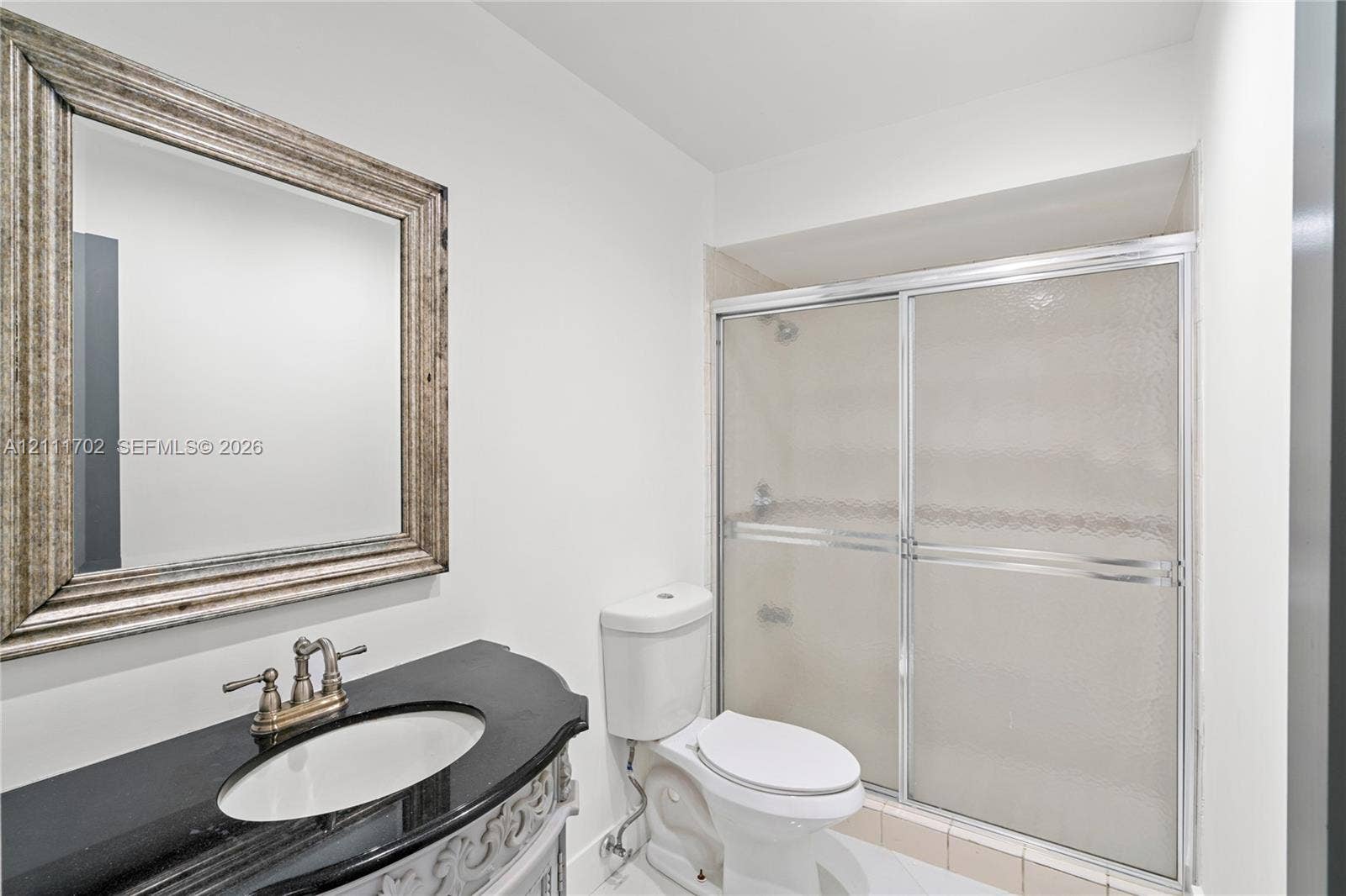 Bathroom featuring a vanity with a dark stone countertop, integrated oval sink, metallic widespread faucet, and a shower enclosure with sliding glass doors