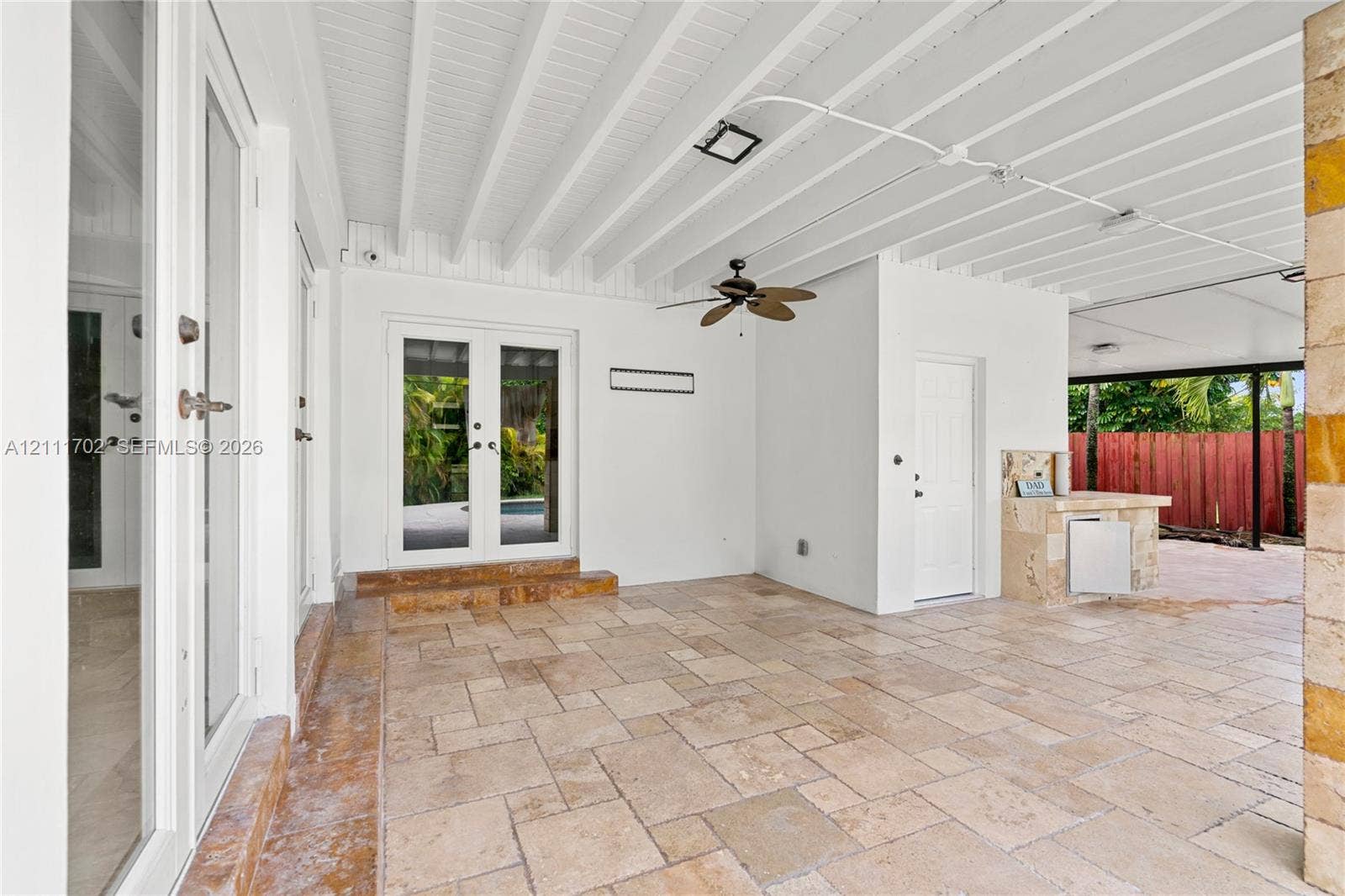 Covered patio featuring stone-tile flooring, exposed beam ceiling with a ceiling fan, and an outdoor kitchenette