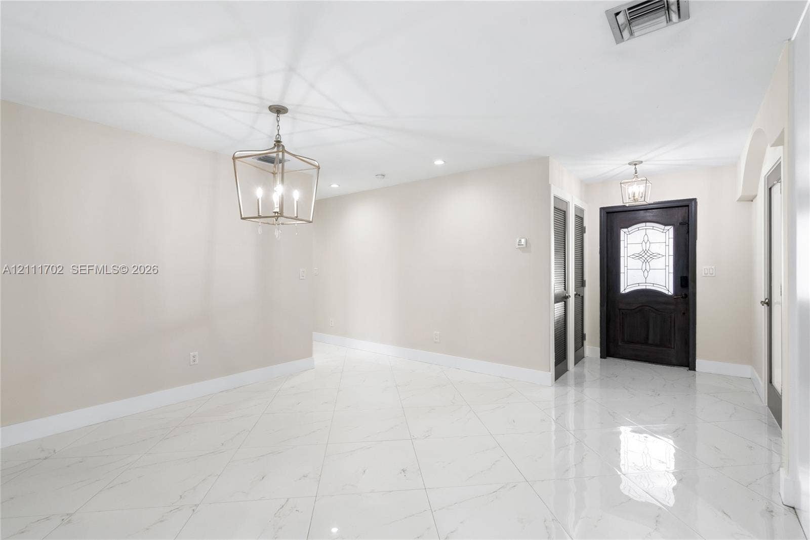 Large-format polished tile flooring, lantern-style chandelier, recessed lighting, and a solid wood entry door with decorative glass inlay