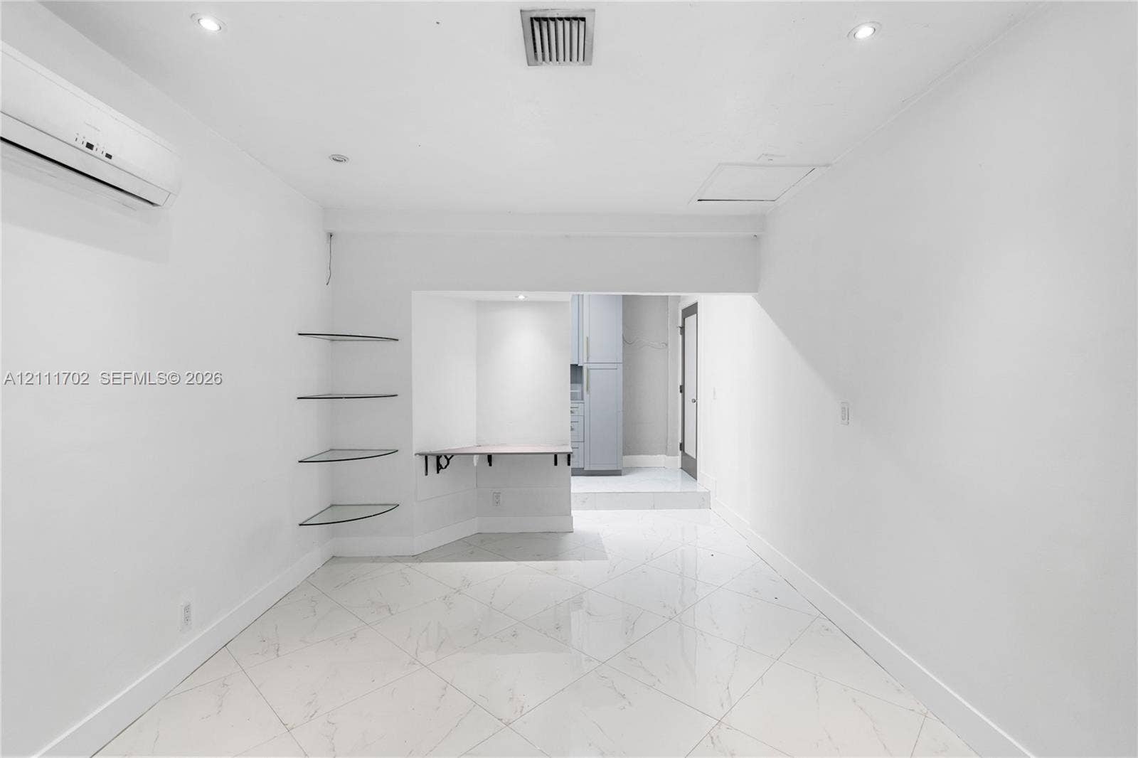 Large-format stone-style tile flooring featuring high-contrast veining, wall-mounted ductless climate control system, built-in glass corner shelving, and recessed ceiling lighting