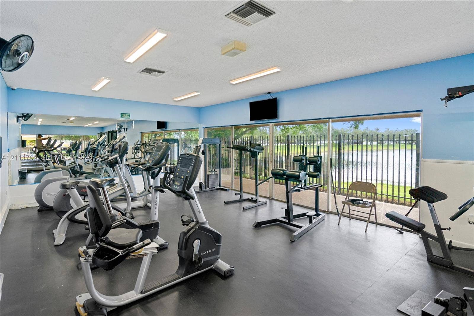 Fitness center featuring rubber flooring, expansive wall-to-wall mirrors, recessed lighting, and floor-to-ceiling glass sliding doors with exterior metal fencing