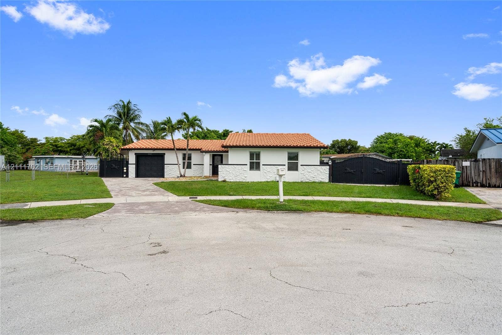 Single-story exterior featuring a clay tile roof, white stucco facade, decorative masonry accent wall, and expansive paved driveway