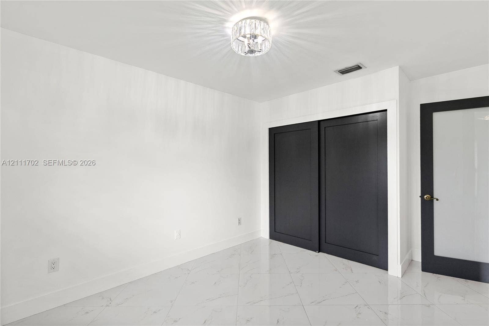 Polished stone-finish tile flooring, matte black sliding closet doors, decorative crystal-style flush mount ceiling lighting, and a solid-core door featuring a frosted glass panel