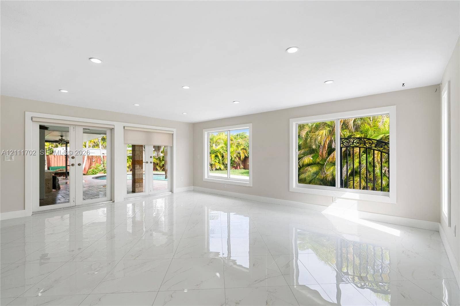 Open-concept interior featuring large-format polished stone-finish tile flooring, recessed ceiling lighting, dual sliding glass doors, and expansive picture windows