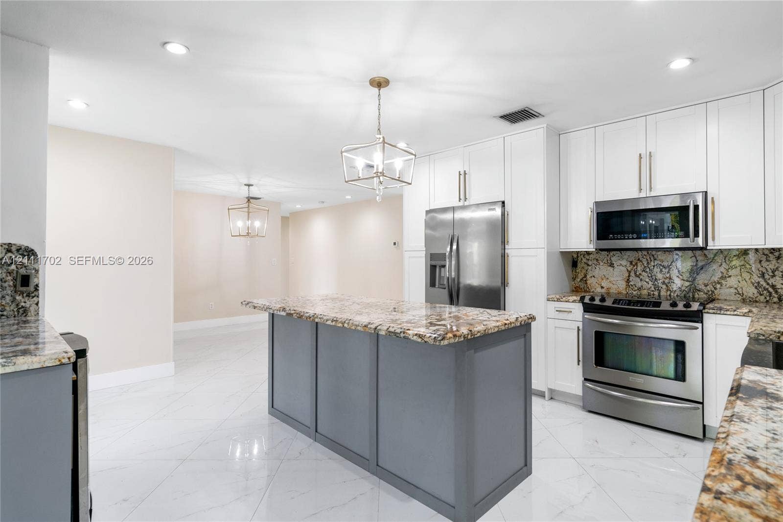 Kitchen featuring white cabinetry, stone countertops, a center island with a grey base, stainless steel appliances, and tile flooring