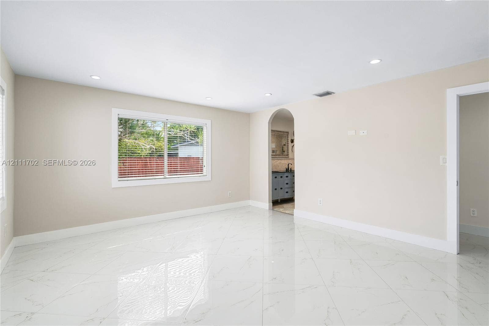 Spacious room featuring polished white tile flooring with veining, recessed lighting, and a prominent arched entryway