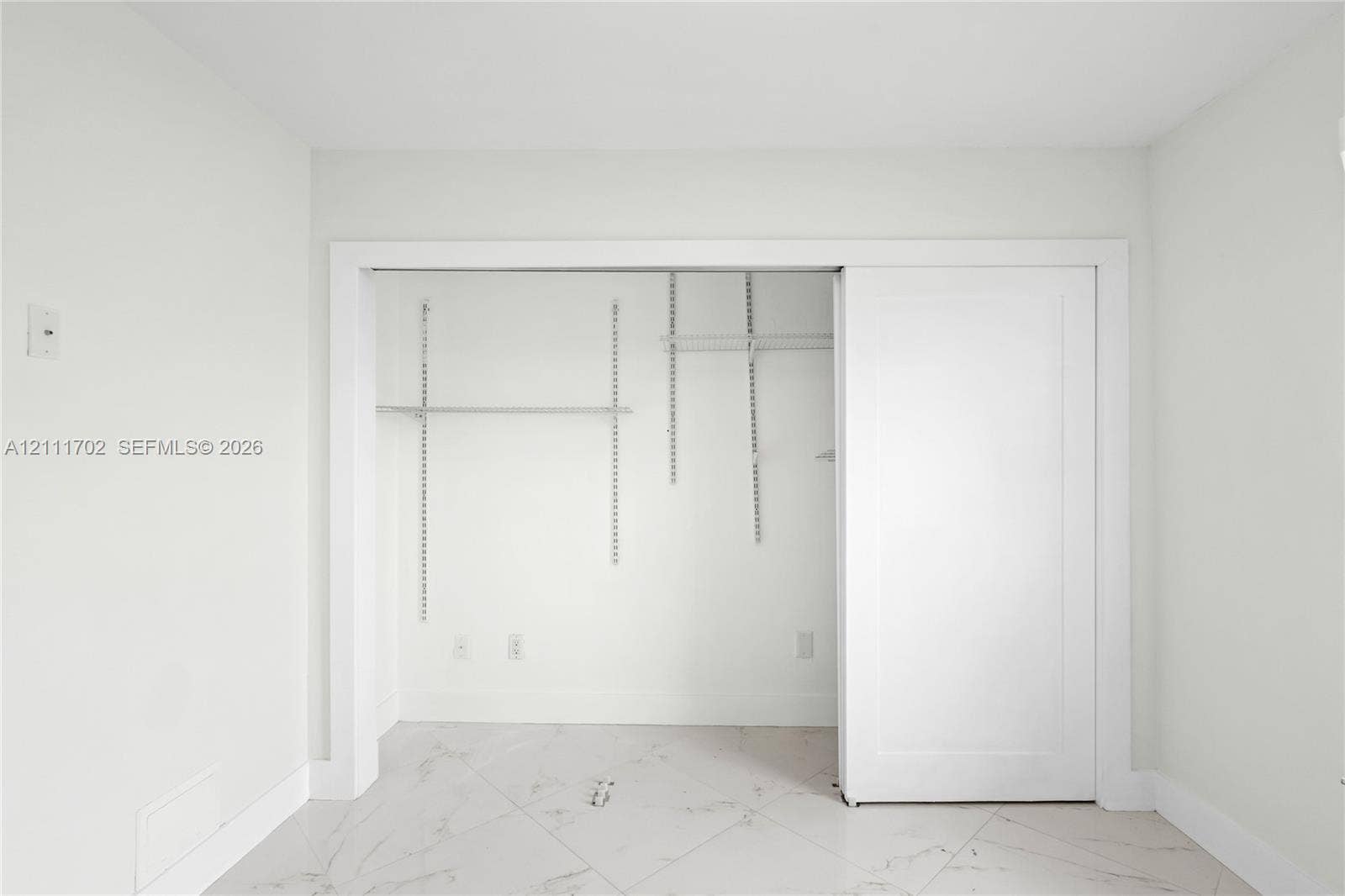 Storage space featuring white sliding doors and interior adjustable wire shelving, set against stone-finish tile flooring