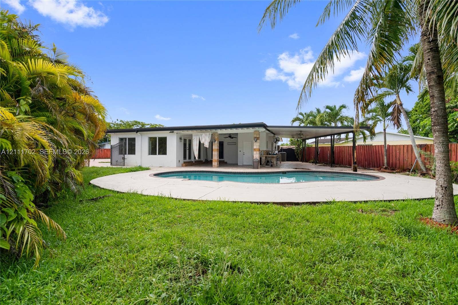 Rear exterior featuring a covered patio, swimming pool with concrete decking, and fenced yard