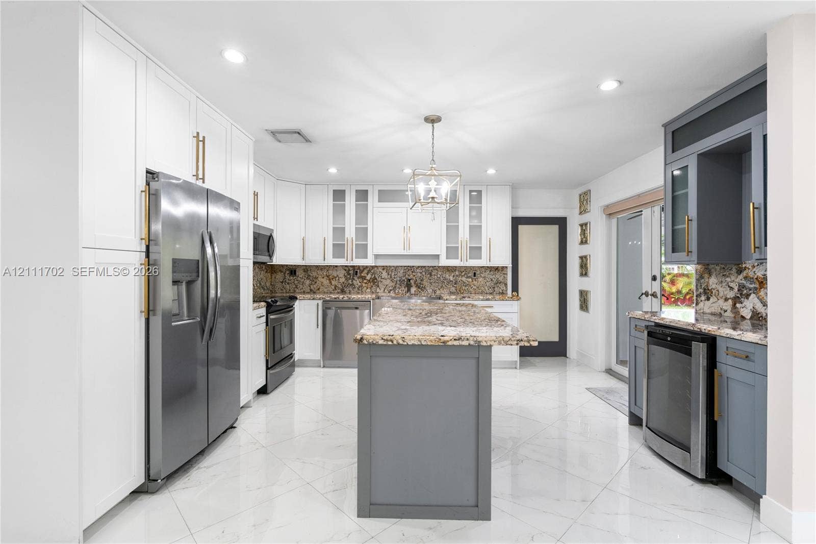 Kitchen featuring white and gray shaker-style cabinetry, stone countertops, central island, stainless steel appliances, and large-format tile flooring