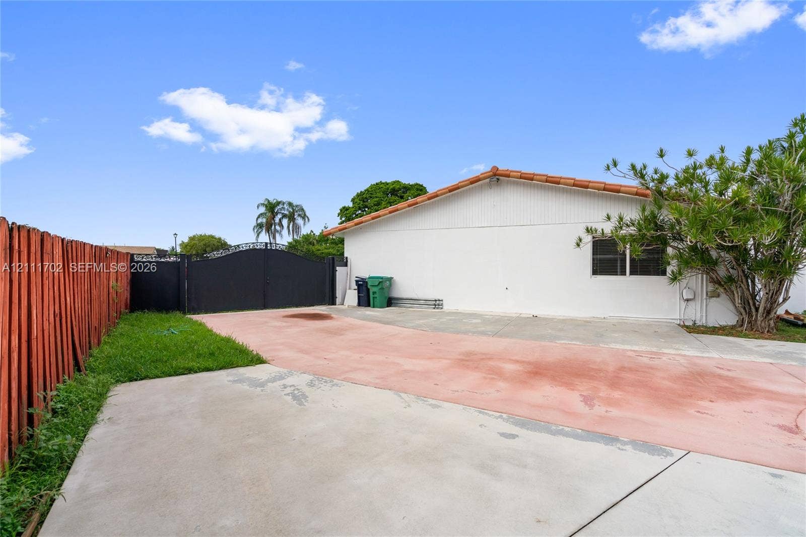Exterior side of property featuring a white stucco facade, terracotta tile roof, concrete parking surface, and gated access